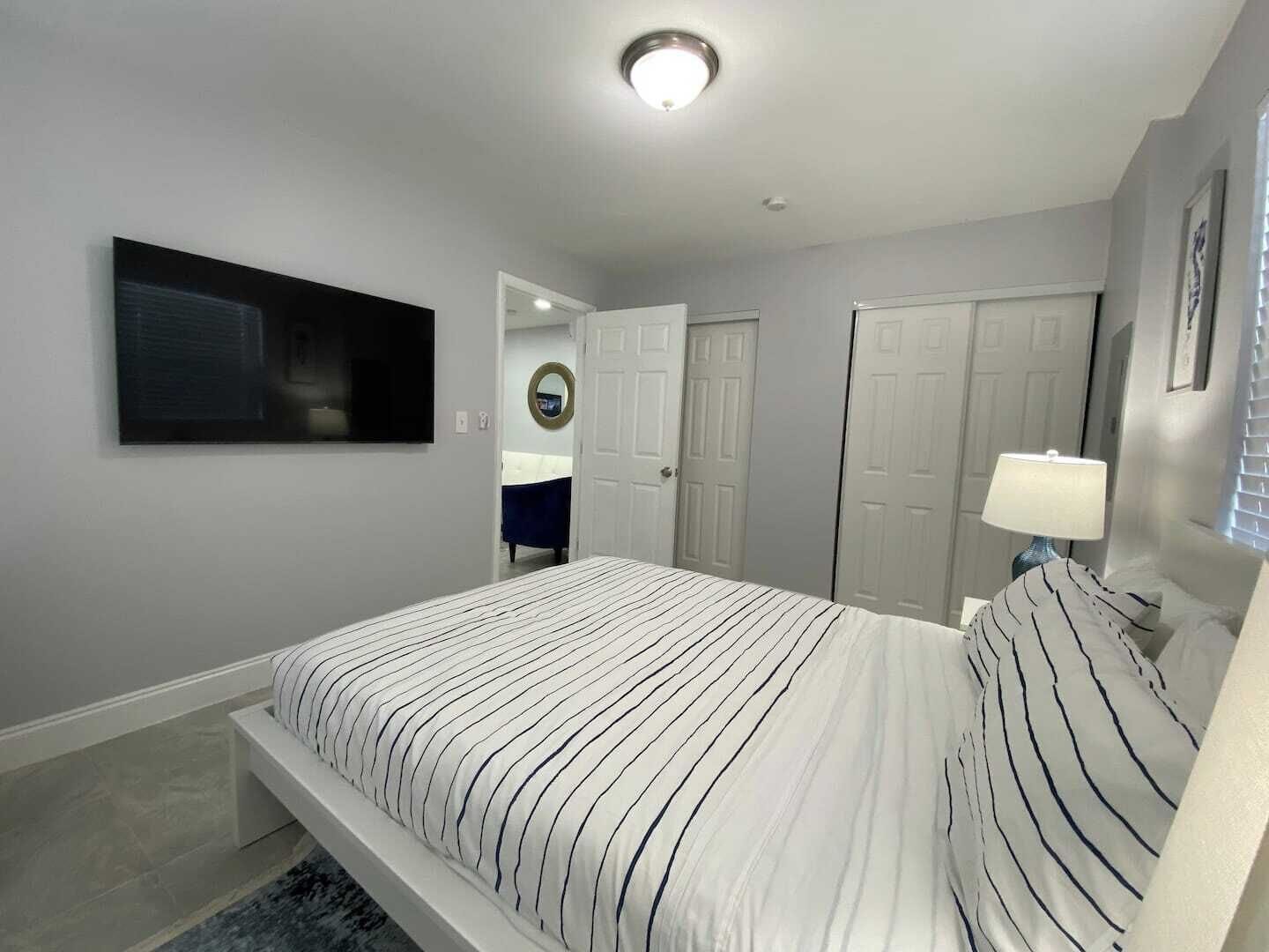 Een slaapkamer met een bed, een aan de muur bevestigde televisie en een deur naar een andere kamer.