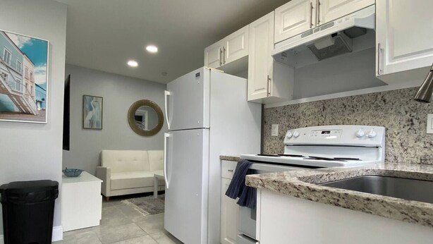 Una cocina compacta con armarios blancos, un refrigerador blanco, una estufa y una encimera de granito.