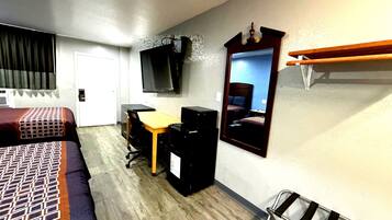 Habitación de hotel con cama, escritorio, silla, computadora, televisor y espejo.