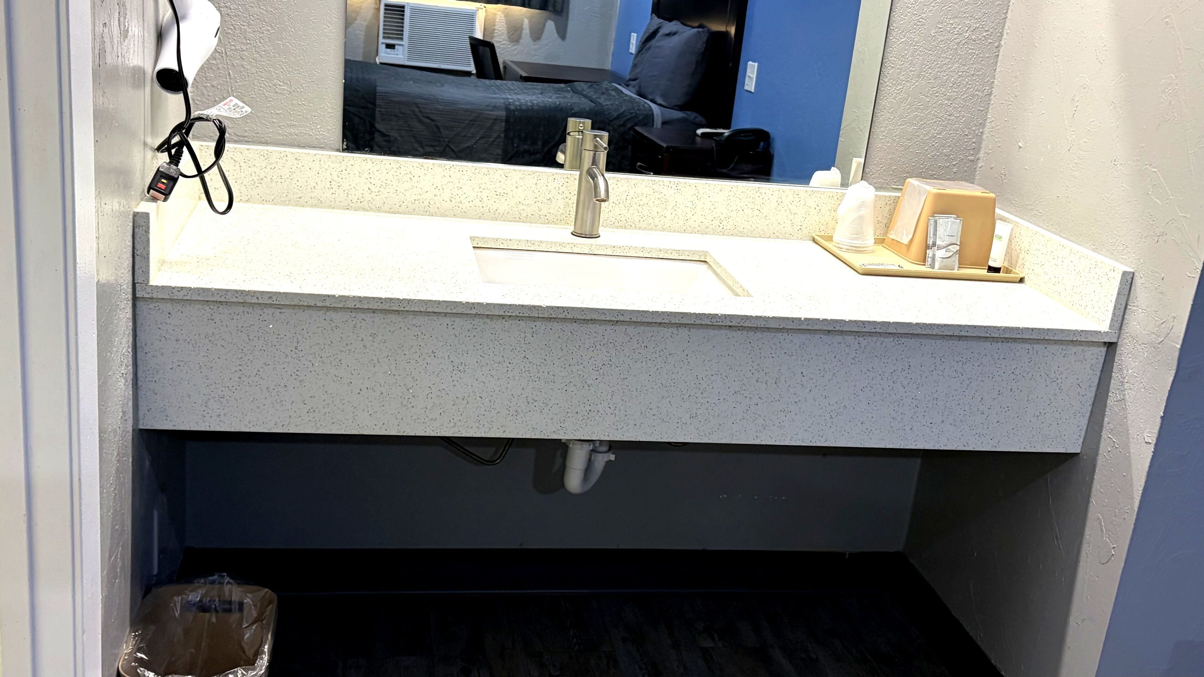A bathroom with a white speckled sink, a mirror, and a visible trash bin.