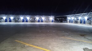 A large, empty parking lot with a row of blue doors and bright lights on the building in the background.
