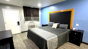 A hotel room with a bed, a bedside table, a nightstand, a wardrobe, and a window with curtains.