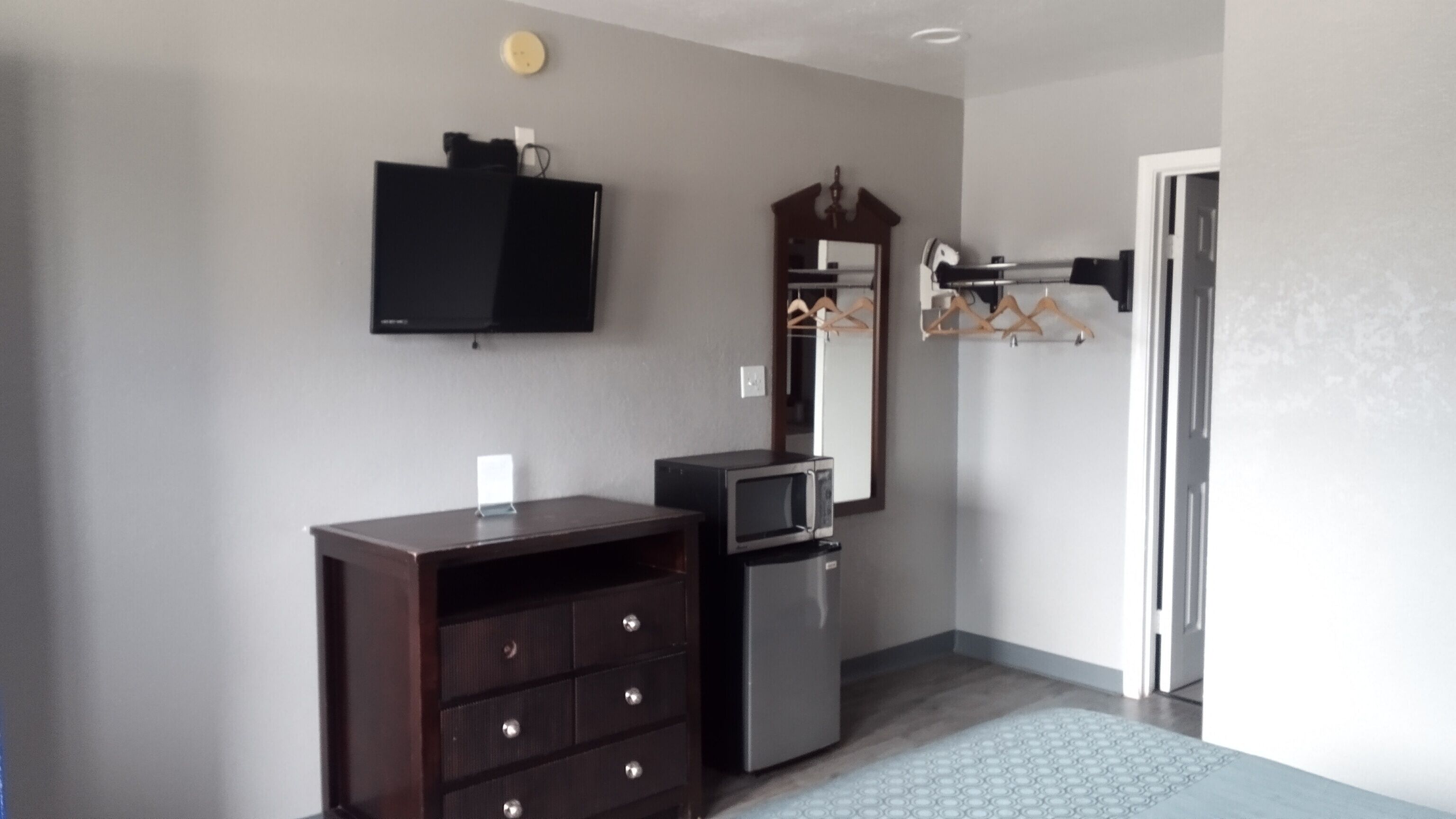 Une chambre avec une commode, un four à micro-ondes, un miroir et un porte-manteau.
