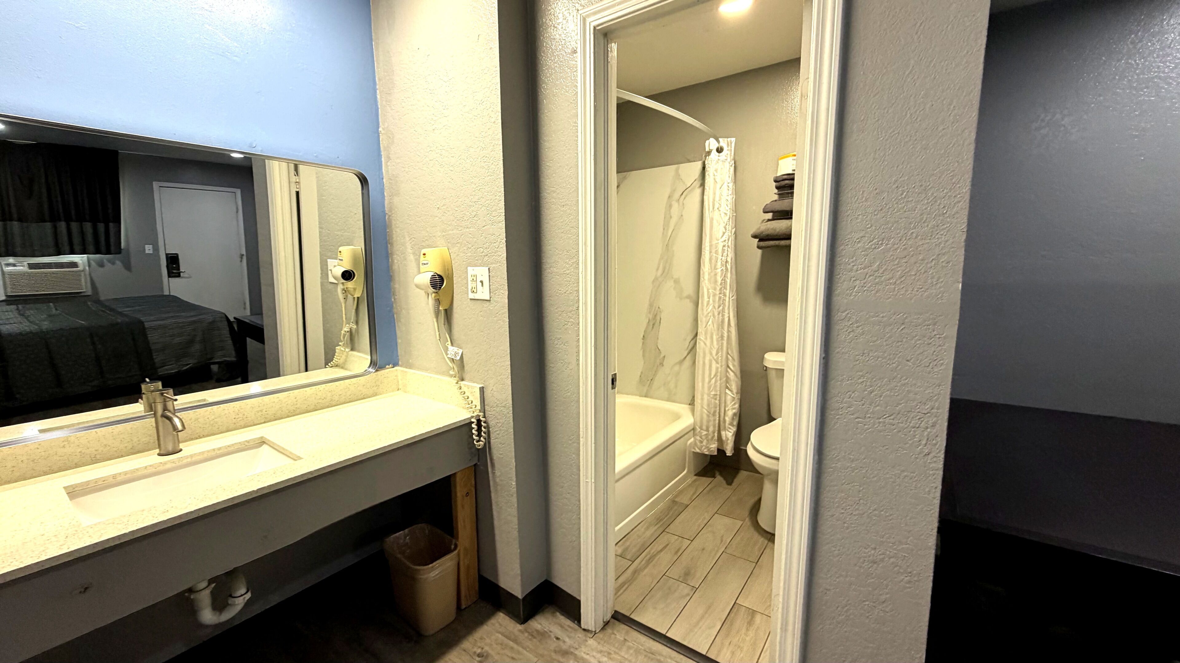 A bathroom with a sink, mirror, hair dryer, and shower.