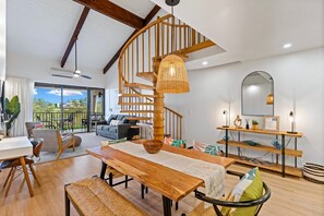 A spacious living area with a wooden spiral staircase, a dining table, and a view of the outdoors.