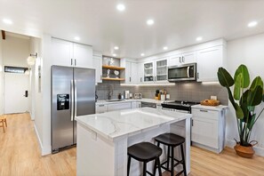 Una cocina moderna con armarios blancos, un refrigerador de acero inoxidable, un microondas y una isla grande con taburetes de bar.