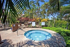Una piscina circular con borde de azulejos, rodeada de palmeras y una valla.