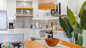 Une cuisine moderne avec des meubles blancs, une machine à café, un grille-pain et une grande plante.