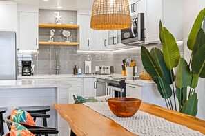 A modern kitchen with white cabinets, a coffee maker, a toaster, and a large plant. - 2BR Kihei Unit with 2 Baths, 3-Zone Split AC, In-Unit Laundry, Pool and Hot Tub! (Kihei)