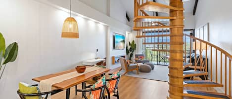 A modern interior with a wooden staircase, a dining area with a wooden table and chairs, and a large window offering a view.