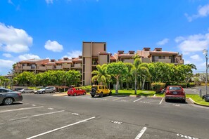 Un hotel de varios pisos con un diseño moderno, que cuenta con balcones y un estacionamiento con varios automóviles.