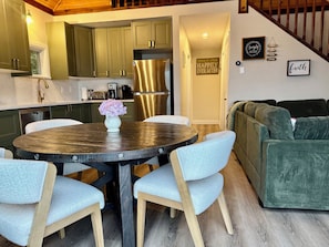 A modern kitchen with green cabinets, a stainless steel refrigerator, and a dining area with a round table and light blue chairs. - Newly renovated Tobermory, Breathtaking Sunset
 (Tobermory)