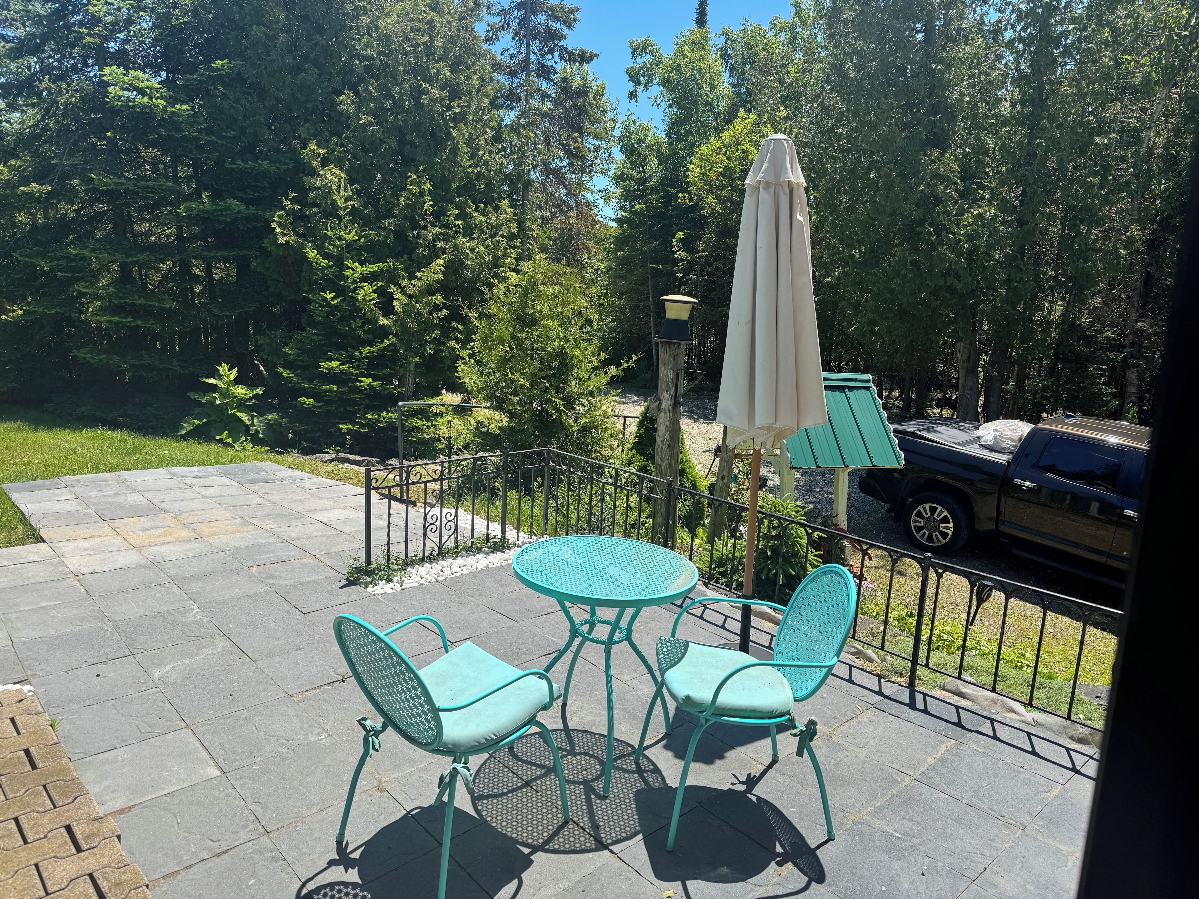 Un patio con una mesa redonda y dos sillas, un toldo y una silla de jardín verde.