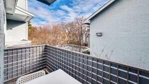 Ein Balkon mit Blick auf ein Schwimmbecken und Bäume, ein weißer Tisch und ein grauer Zaun.