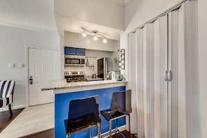 A compact kitchen with a built-in microwave, stove, and sink, featuring blue cabinets and a small bar area with two chairs.
