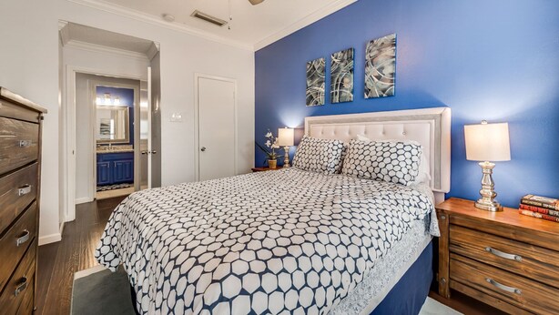 Un dormitorio con una cama, mesitas de noche, un ventilador de techo y cuadros en la pared.