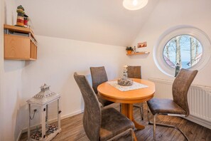 Een eetruimte met een ronde tafel, vier stoelen, een klein kastje en een raam met uitzicht.