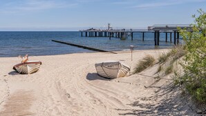 Una platja amb dos vaixells, un moll i un cel clar.