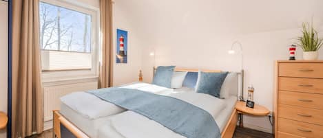 A bedroom with a bed, bedside tables, a dresser, a window with curtains, and a wall-mounted picture.