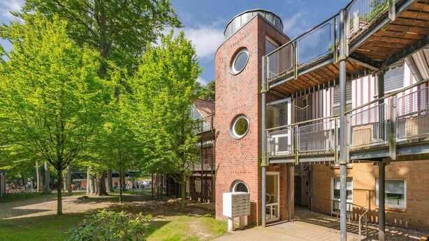 Ein Innenhof mit einem Backsteinhaus, einem Baum und einer Metallbalkonkonstruktion.