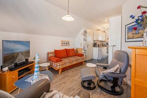 Una sala de estar con televisor, sofá, sillón y una mesita con un objeto decorativo.