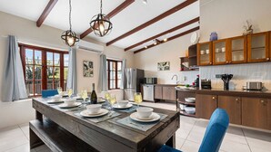 A dining area with a wooden table set for a meal, a kitchen with wooden cabinets, and a view of the outdoors through large windows. - ~Sleeps 12 ~Spacious ~Private Pool ~Great Location (Noord)