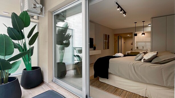 Een moderne slaapkamer met een groot bed, een schuifdeur naar een balkon en potplanten.