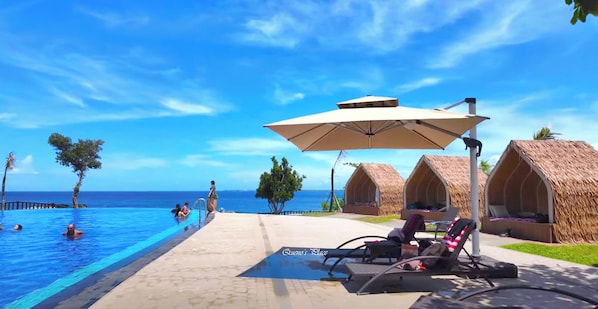 A poolside area with lounge chairs and umbrellas, a clear blue sky, and a view of the ocean.
