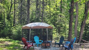 Un camping con una zona de comedor cubierta, mobiliario exterior y una chimenea.