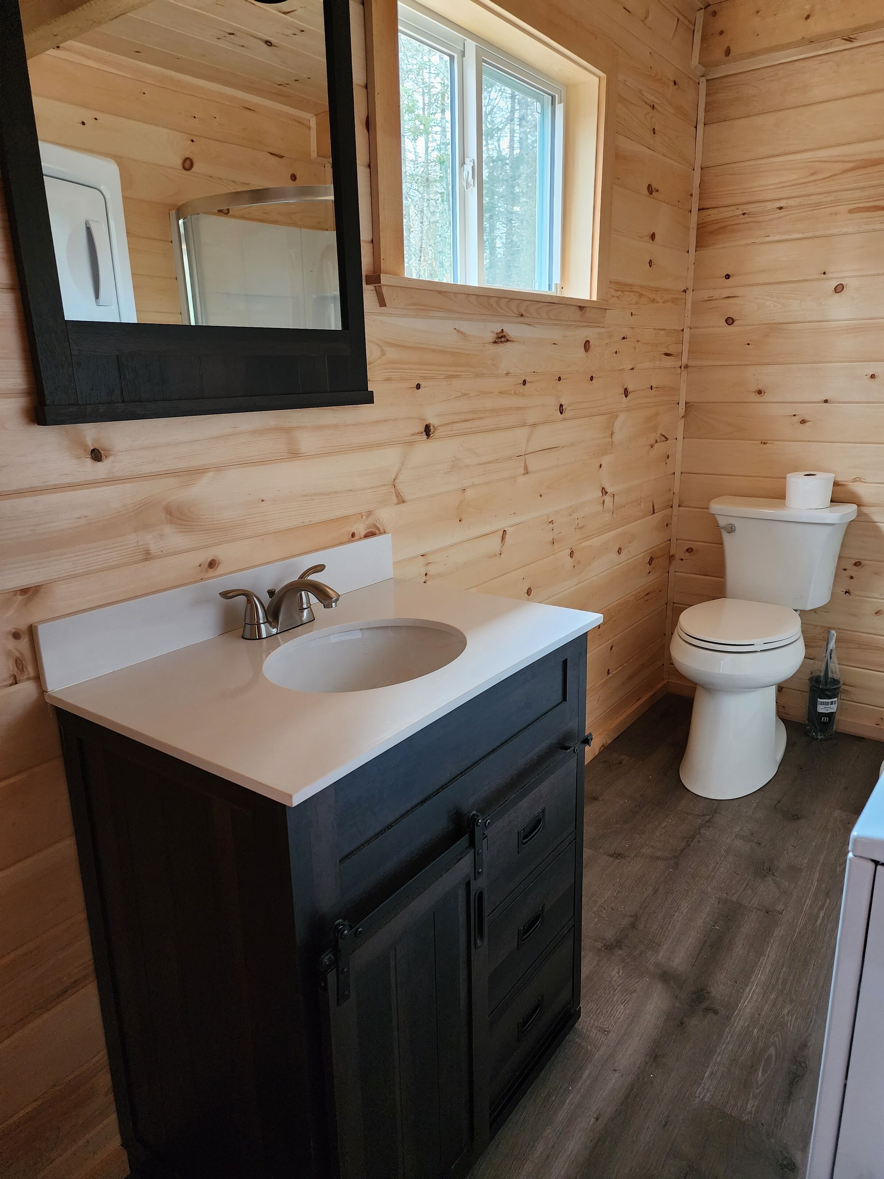 A wooden cabin bathroom with a white sink, black cabinets, a mirror, and a toilet.