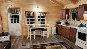 Una cocina acogedora de estilo cabaña, con paredes de madera, una mesa de comedor con dos sillas, un lavamanos y una estufa.