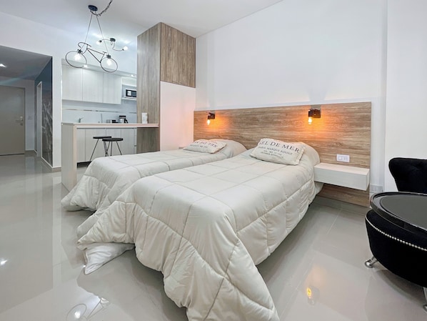 A modern hotel room with two beds, a desk, and a chair.