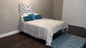 A bedroom with a bed, a headboard, a patterned rug, and a door.