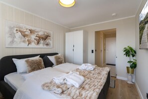 A modern hotel room with a large bed, a painting on the wall, a wardrobe, and a potted plant. - Playa - Schönes 1-zimmer App., Strandnah, Balkon, Wlan. Haustiere Erlaubt (Westerland)