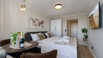 Hotelkamer met een bed, een eettafel met een champagnefles, een stoel, een schilderij aan de muur en een plant.