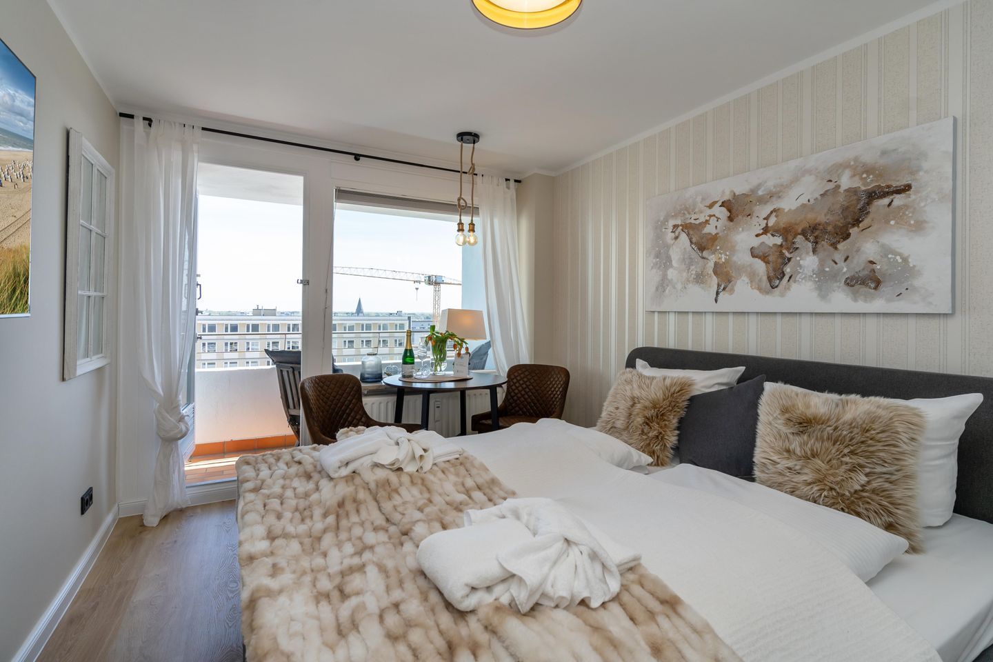 A hotel room with a bed, a dining table, chairs, a view of the city, and a large abstract painting.