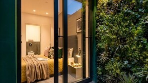 Un dormitorio con cama, mesita de noche, lámpara y pared verde con plantas.