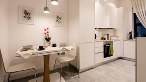 Una cocina moderna con armarios blancos, una mesa de comedor con sillas, lámparas colgantes y un florero con flores.