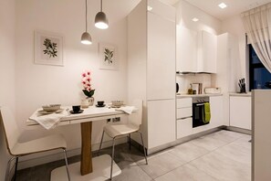 Una cocina moderna con armarios blancos, una mesa de comedor con sillas, lámparas colgantes y un florero con flores.