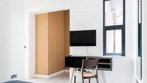 Una habitación moderna con un armario de madera, un escritorio con una silla, un televisor de pantalla plana y una ventana.