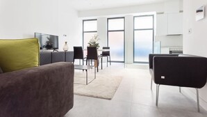 Una sala de estar moderna con sofá, sillas, una mesa de centro y televisor. Se ve una ventana grande con vista al cielo.