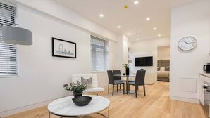 Un salon moderne et bien éclairé, comprenant un coin repas, un canapé, une table basse et un téléviseur fixé au mur.
