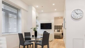 Un salon moderne comprenant un coin repas, un téléviseur fixé au mur et une horloge.