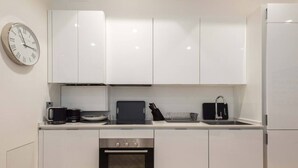 Une cuisine moderne avec des armoires blanches, un four en acier inoxydable, une machine à café et une horloge au mur.