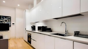 Una cocina moderna con gabinetes blancos, un lavamanos de acero inoxidable y una cafetera negra.