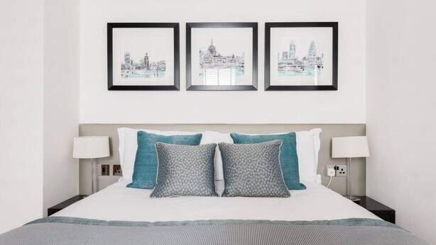 Habitación de hotel con una cama, dos lámparas de noche y tres cuadros con vistas de la ciudad en la pared.