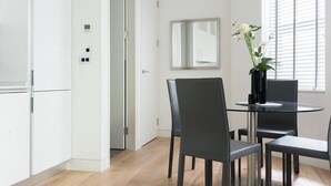 Una cocina moderna con armarios blancos, una mesa de vidrio con cuatro sillas, y una planta en maceta sobre la mesa.