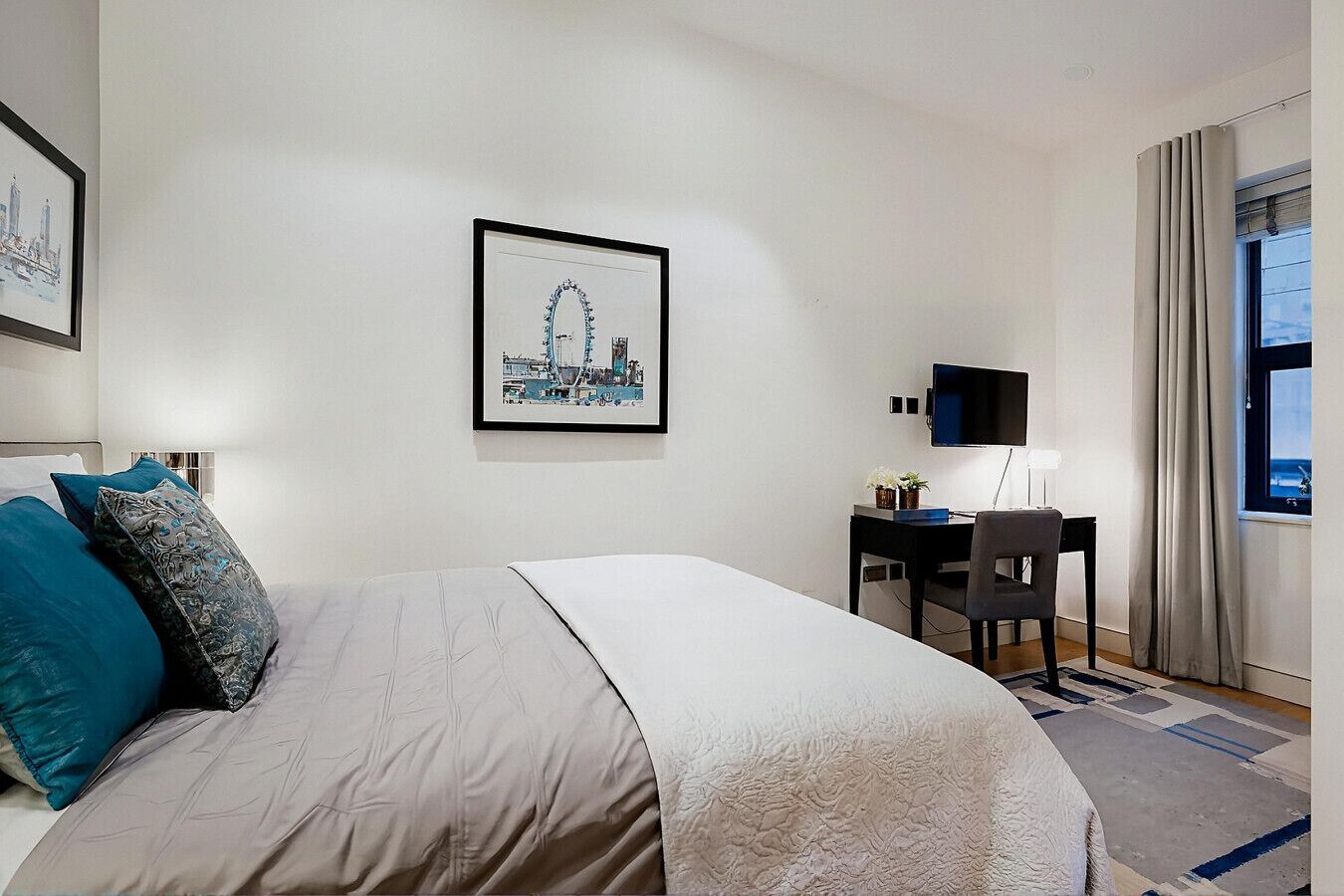 A hotel room with a bed, a desk, a chair, a TV, and a window with curtains.