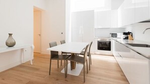 A modern kitchen with white cabinets, a dining table with chairs, and a wooden floor.