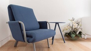 A blue armchair with metal legs, a small table, and a potted plant with white flowers.